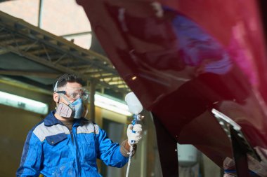 Portrait of man wearing protective mask painting boat using paint sprayer in yacht workshop at factory clipart