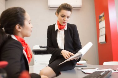 Siyah ve kırmızı üniforma oturan meslektaşım modern Office belgeleri gösterilen masa üzerinde giyen genç ve güzel iş Danışmanı portresi