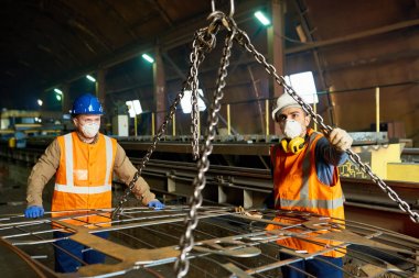 Çelik fabrikası giyen üniforma ve Filtre maskeleri ağır metal levha, arka plan üzerinde üretim bölümünün iç taşımada kaldırma ışını kullanarak iki genç işçileri