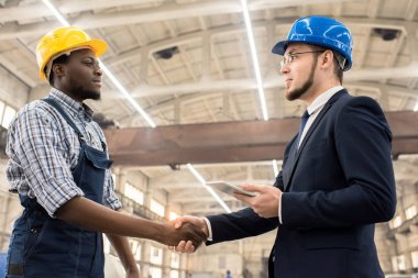 Tulum giymiş yakışıklı Afro-Amerikan işçi ve hardhat duran firma el sıkışma ile kendine güvenen yatırımcı modern bitki geniş üretim departmanı tebrik