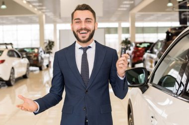 Portre yakışıklı araba satıcısı bir holding araba anahtarları ve neşeyle kamera ayakta lüks Bayilik showroom gülümseyen