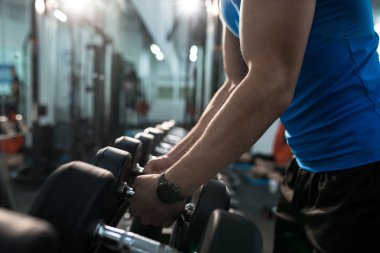 Yan görünümü yakın güçlü erkek el dumbbells ekipmanlardan tespit ayağa modern spor salonu, kopya alanı