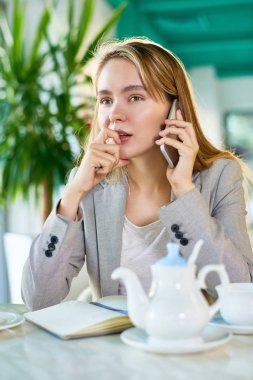 Kafeterya masada oturan ve onun meslektaşım için smartphone, bel, dikey konuşurken sarı saçlı işkadını konsantre