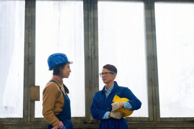 İki kadın işçilerin endüstriyel atölye penceresinde karşı ayakta sohbet portre kadar bel