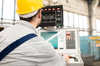 Cnc makine, iç arka plan üzerinde üretim bölümünün önünde oturma sırasında iş sakallı operatörü koruyucu miğfer arkadan görünüm odaklı