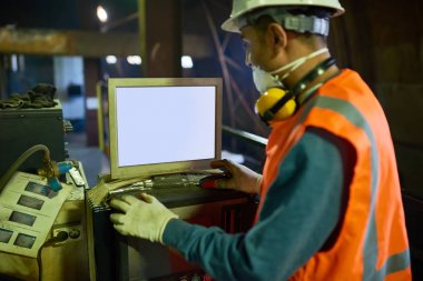 Filtre maskesi ve kask takıyor kendine güvenen genç operatör iş Cnc makine, iç arka plan üzerinde geniş üretim bölümünün önünde dururken üzerinde duruldu