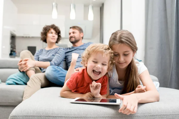 兄と妹デジタル タブレットを使用して バック グラウンド コピー スペースでテレビを見て両親とリビング ルームのソファの上に横たわっている間笑いの肖像画 — ストック写真