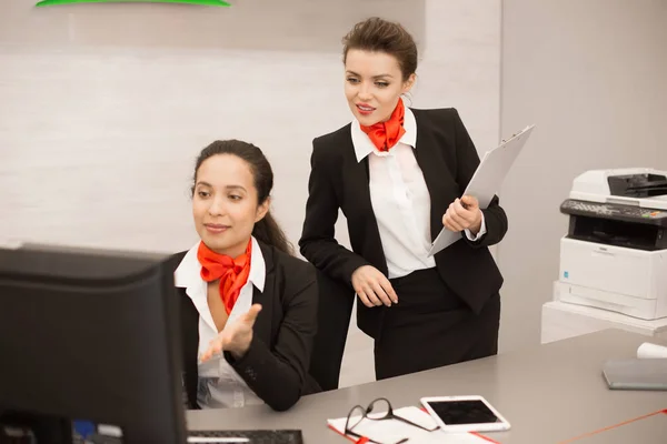 两个漂亮的女商人的肖像穿着黑色和红色制服使用电脑在办公桌上的现代办公室搜索工作网络 — 图库照片