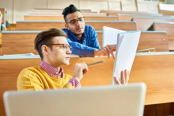 两个年轻男子的低角度看 其中一个中东坐在办公桌在现代演讲厅在大学和分享笔记 — 图库照片
