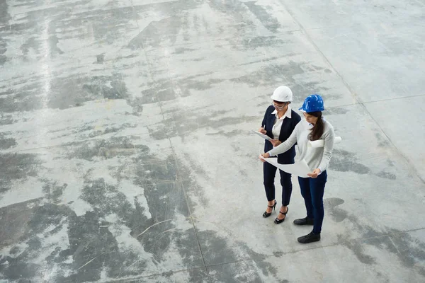Wysoki Kąt Widzenia Dwóch Inżynierów Kobiet Noszenie Budowlani Zbadanie Planów — Zdjęcie stockowe