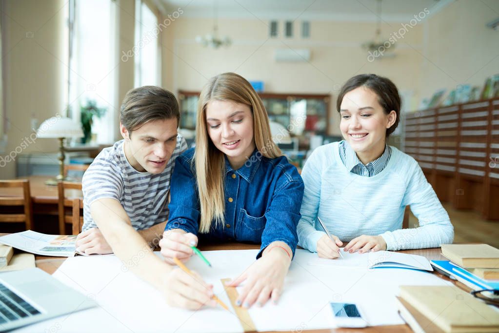 Talented university students wrapped up in discussing research work while sitting at wooden desk of spacious library, attractive girl with charming smile listening to her groupmates with interest