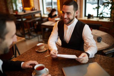 Kafe 'deki iş görüşmesi sırasında ortağımla konuşurken mutlu bir şekilde gülümseyen başarılı sakallı işadamının yüksek açılı portresi.