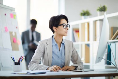 Ofiste otururken bilgisayar kullanan başarılı genç iş kadınının yan görünüm portresi.