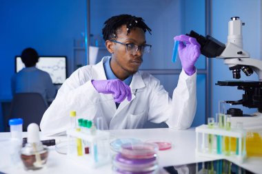 Laboratuvarda tıbbi araştırmalar üzerinde çalışırken deney tüpü örnekleri tutan Afro-Amerikalı genç bir adamın portresi.