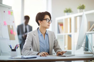 Ofiste otururken bilgisayarını kullanan başarılı genç iş kadınının yan görünüm portresi.