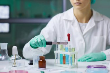 Tıp laboratuarında araştırma yaparken renkli sıvıyla test tüpü alan tanınmayan bir kadının yakın çekimi.