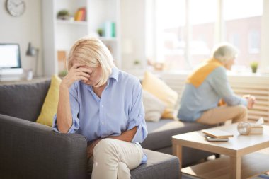 Evde karşı koltukta oturan yaşlı çiftin portresi, ön plandaki hayal kırıklığına uğramış eşe odaklan, ön plandaki boşluğu kopyala.