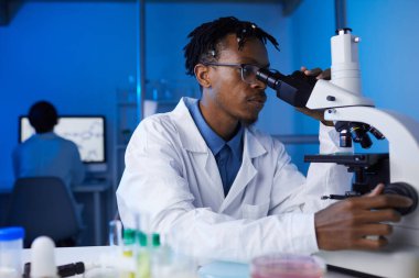 Laboratuvarda tıbbi araştırmalar yaparken mikroskopla bakan genç Afro-Amerikan bir adamın portresi.