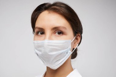 Kadın doktorun koruyucu maske taktığı ve beyaz arka planda poz veren kadın portresi.
