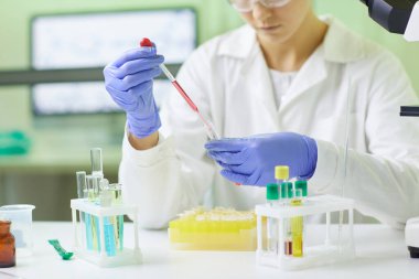 Genç kadın bilim adamının tıbbi laboratuarda çalışırken damlatıcıyı kullanarak kan testi örneği hazırladığı yakın plan.