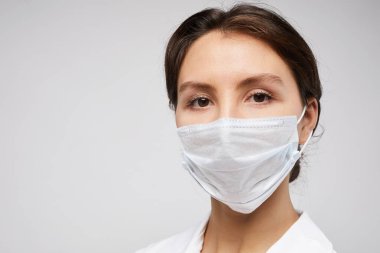 Koruyucu maske takan ve beyaz arka planda poz veren kadın doktorun kafa ve omuz portresi.