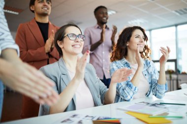 Low angle portrait of creative team clapping happily while celebrating success in office, focus on two smiling young women in foreground