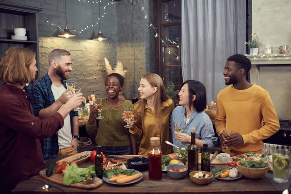 多民族笑容满面的年轻人一起吃完饭 站在现代室内餐桌旁 举着酒杯 复制空间 — 图库照片