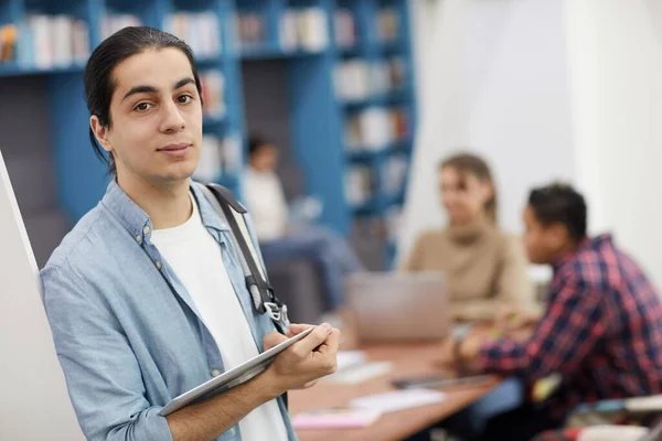 Waist up portrait of long-haired college student looking at camera while standing in modern library, copy space