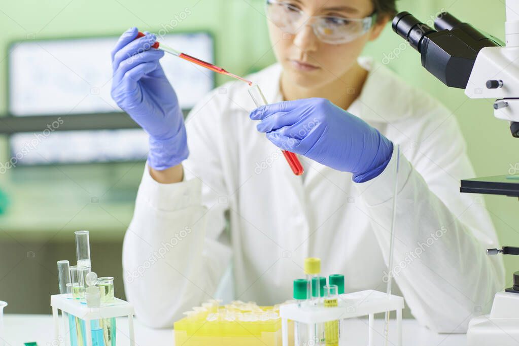 Cropped portrait of young female scientist preparing blood test sample using dropper while working in medical laboratory, copy space