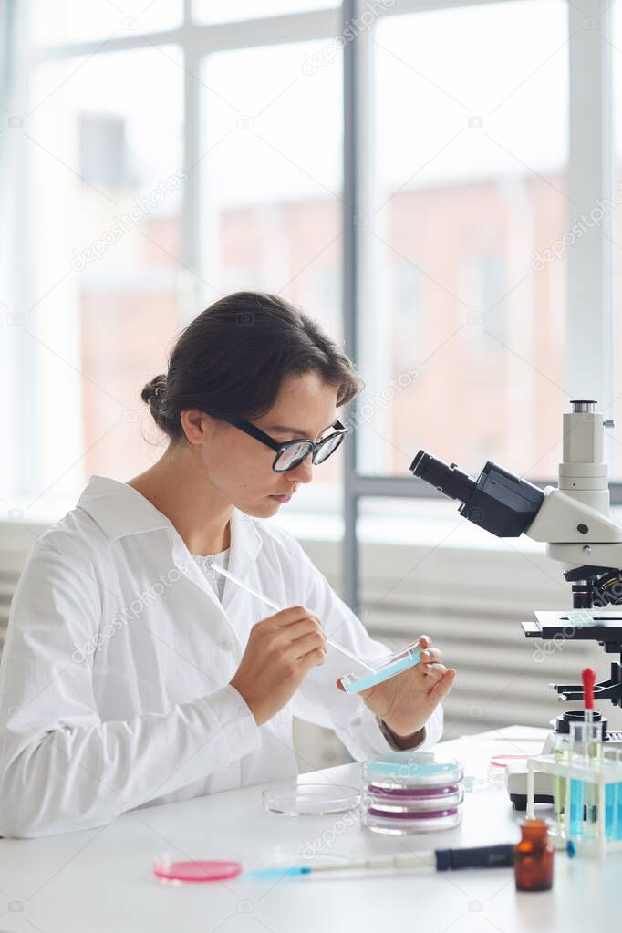 Side view portrait of beautiful young woman working in laboratory, preparing test samples in petri dish for microscope research, copy space