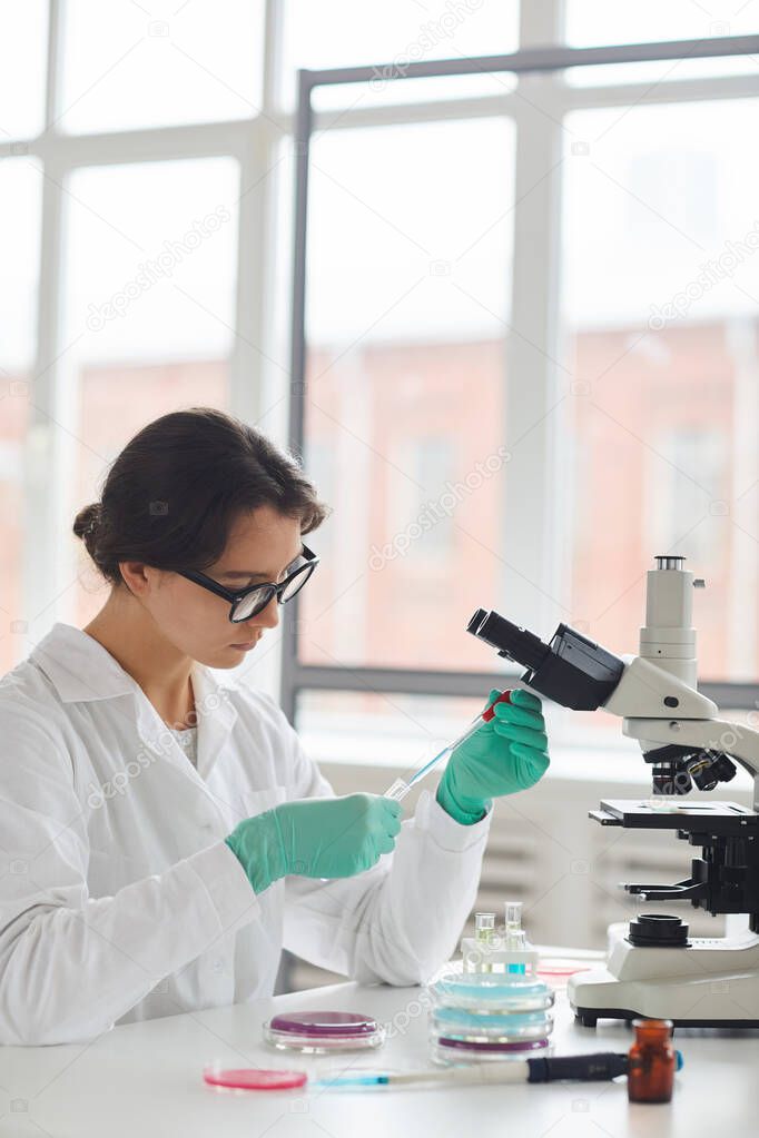 Side view portrait of beautiful young woman working on research in medical laboratory and preparing test samples sitting by window