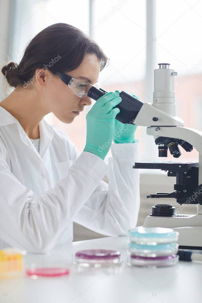Side view portrait of beautiful young woman looking in microscope while working in medical laboratory