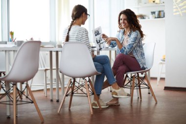 Çağdaş iki genç kadının tam boy görüntüsü mutlu bir şekilde gülümserken masada otururken pencerenin karşısında, boşluğu kopyala