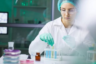 Tıp laboratuarında araştırma yaparken renkli sıvıyla test tüpü kullanan genç bir kadının portresi.