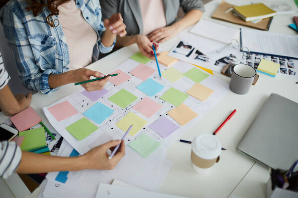 High angle view of creative team planning startup project on table, focus on hands pointing at colorful sticky notes during meeting, copy space
