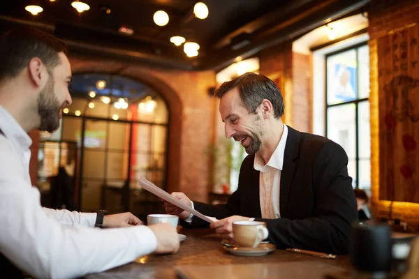 Side view portrait of two successful business people signing contract while sitting at table in luxurious cafe, copy space