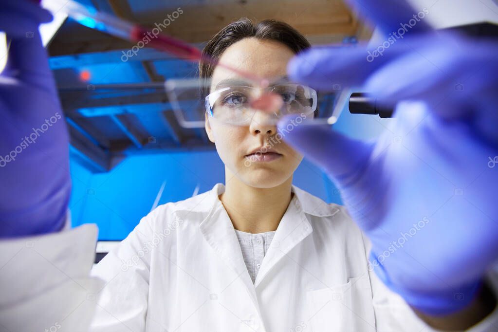 Low angle view at young female scientist preparing test sample using dropper while working in medical laboratory, copy space
