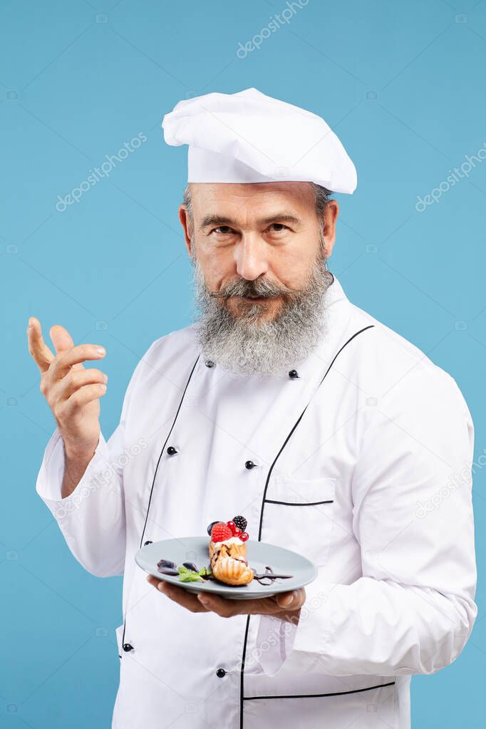 Waist up portrait of charismatic bearded chef presenting beautiful dessert while standing against blue background