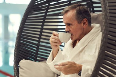 Lüks Spa Otel 'deki şezlongda dinlenen ve kahve içen varlıklı yaşlı adamın yan görünümü.