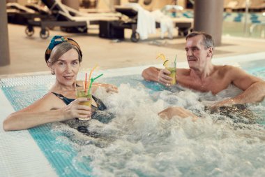 Modern yaşlı çiftin yüksek açılı portresi kabarcıklı jakuzide dinleniyor ve lüks Spa Otel 'de kokteyl içiyor, fotokopi çekiyor.