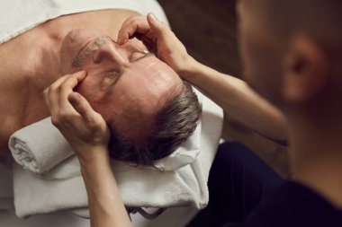 Lüks Spa Merkezi 'nde yüz masajından zevk alan yakışıklı bir adamın yüksek açılı portresi.