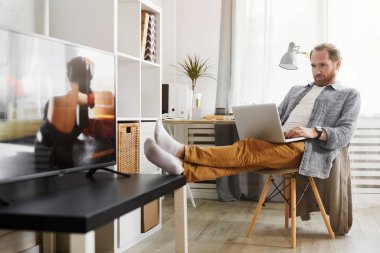 Evde dinlenirken dizüstü bilgisayar kullanan yakışıklı bir adamın tam boy portresi, boşluğu kopyala