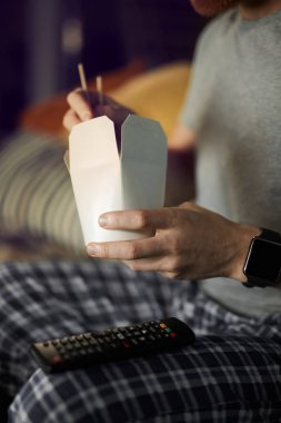 Karanlıkta TV seyreden ve gece filmlerinin tadını çıkarırken dışarıdan erişte yiyen tanınmamış bir adamı yakından çek.