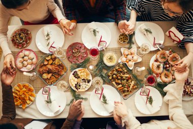 Above view at group of people sitting at dining table on Christmas and joining hands in prayer, copy space clipart