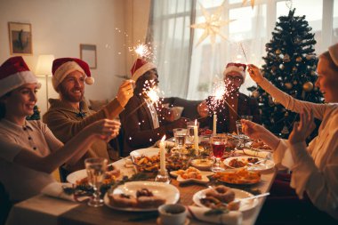 Multi-ethnic group of people raising glasses while enjoying Christmas dinner at home clipart