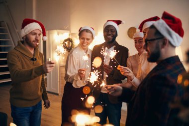 Çok ırklı bir grup insan ellerinde parlak ışıklar tutarken Noel kutlamalarının keyfini çıkarıyorlar.