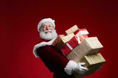 Gülümseyen Noel Baba 'nın belindeki portre kırmızı arka planda hediyeler taşıyor.