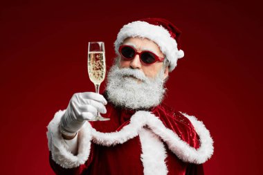 Modern Noel Baba 'nın kırmızı arka planda dururken elinde şampanya bardağı olan belini kaldır ve boşluğu kopyala.