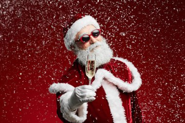 Havalı Noel Baba 'nın belindeki portre şampanya bardağını tutarken kırmızı arka planda kar yağarken, kopyalama alanı