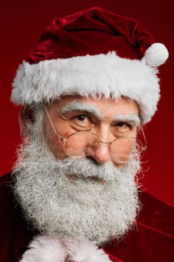 Peri masalı Noel Baba 'nın başı ve omuzları kırmızı arka planda poz verirken kameraya nazikçe bakıyor.